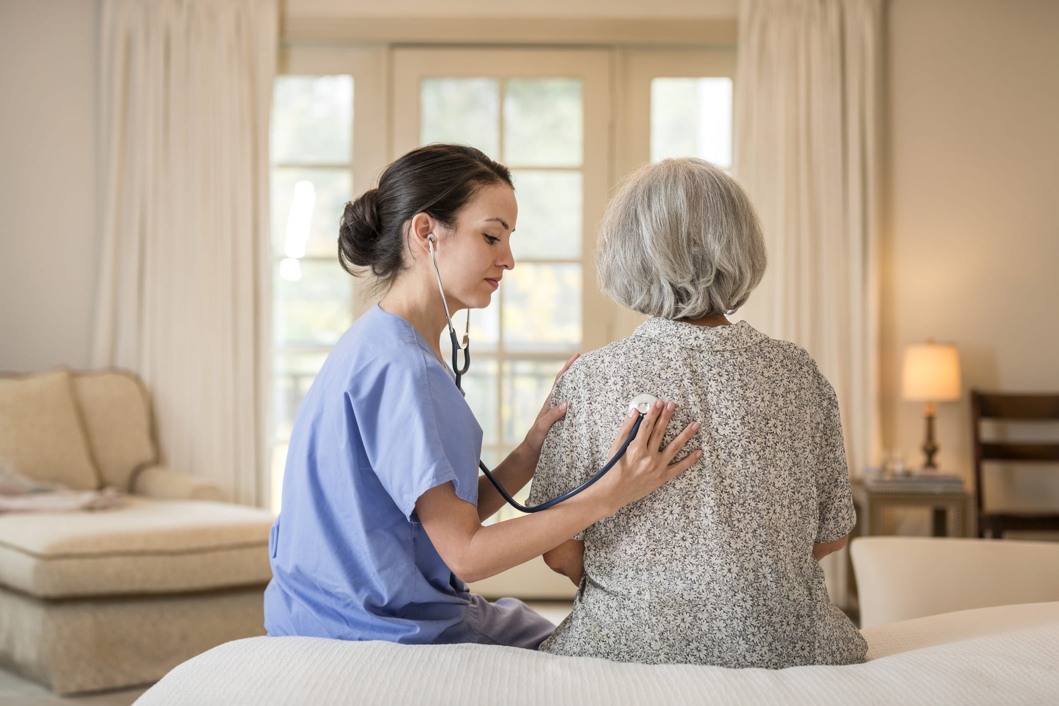 Nurse listening to chest of patient in home