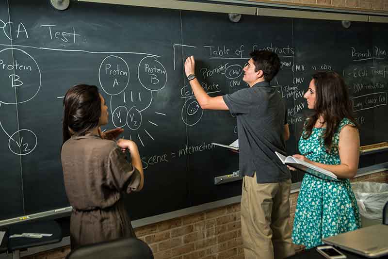 three students writing on a chalkboard