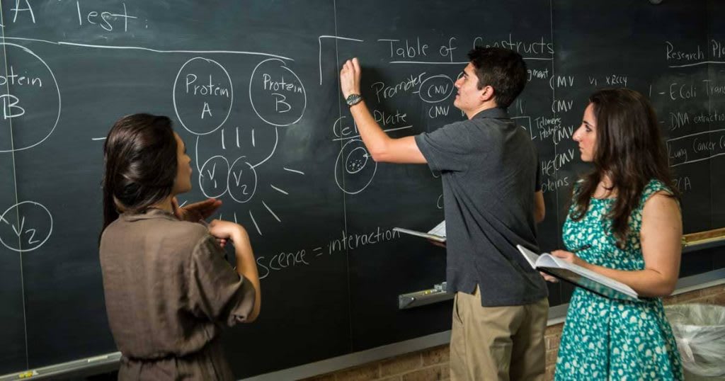 three students standing at black board