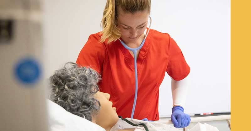 Nurse in red scrubs working with sim manikin