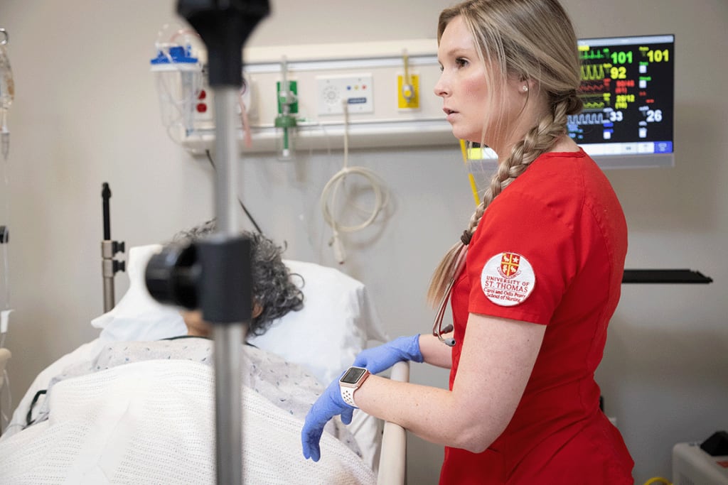 UST ABSN student standing by sim manikin in lab bed