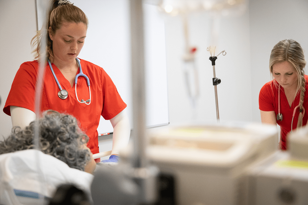 nursing students in red scrubs working in lab