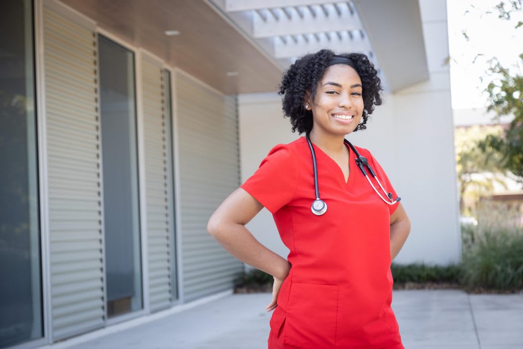 nursing student in red scrubs standing outside