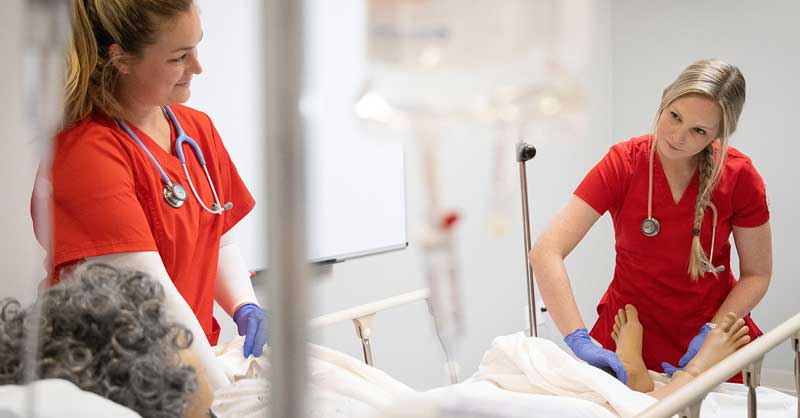 UST nursing students with red scrubs working with a simulation manikin