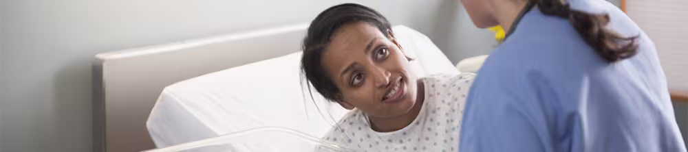A nurse assists a woman in a hospital bed and a newborn baby