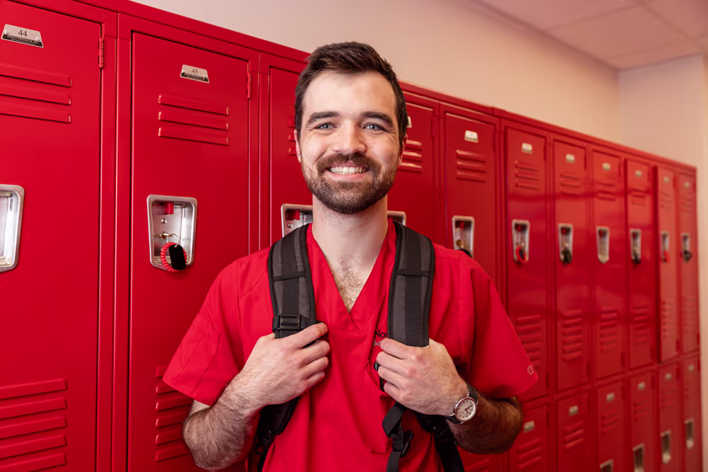 Nursing student wearing backpack and standing in front of lockers