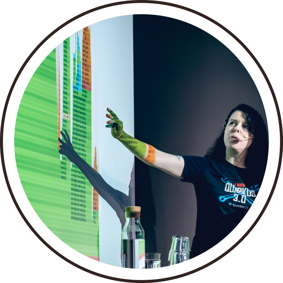 A speaker gesturing towards code on the screen behind her.