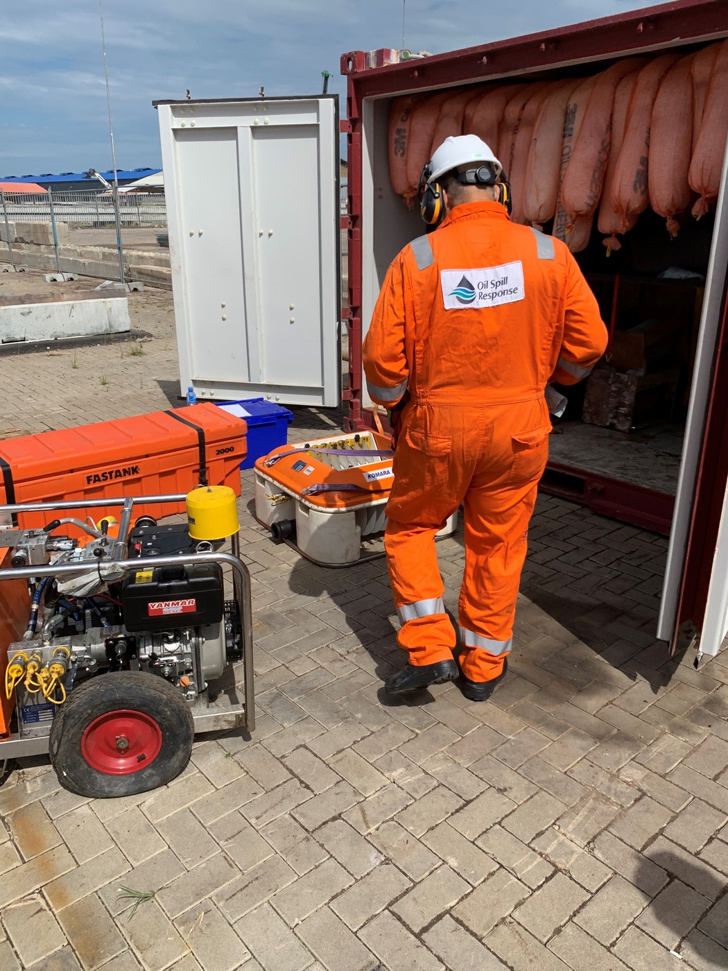 An OSRL responder in an orange safety suit and hard hat examines oil spill containment equipment stored in a response container. The image highlights preparedness efforts in Suriname’s oil and gas sector.
