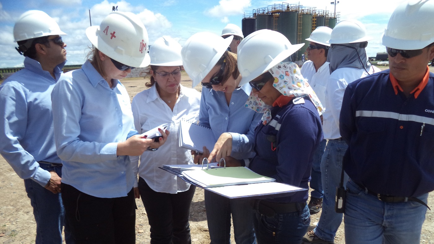 A site inspection team wearing hard hats and safety gear examines printed contingency plans outdoors, symbolising cross-functional collaboration, stakeholder engagement, and real-world implementation of oil spill readiness procedures.