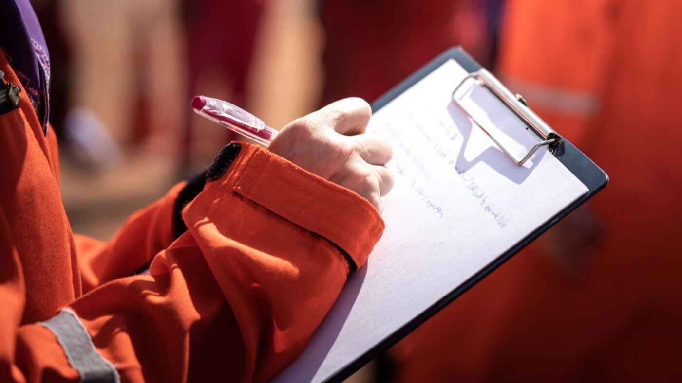 A close-up of a responder in high-visibility gear writing on a clipboard during an exercise—capturing real-time assessment vital for contingency planning and improvement tracking.