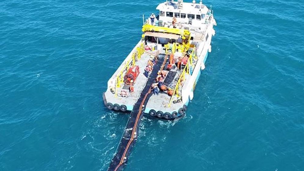 An offshore oil spill response vessel deploying a long containment boom into the water to prevent the spread of oil, showcasing critical containment techniques during emergency exercises.