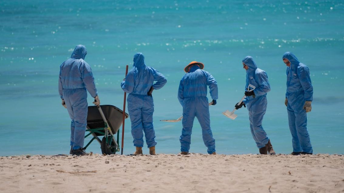rained emergency response personnel in protective suits carefully conducting a shoreline cleanup, ensuring safe and effective oil spill remediation efforts along the Western Australian coast.