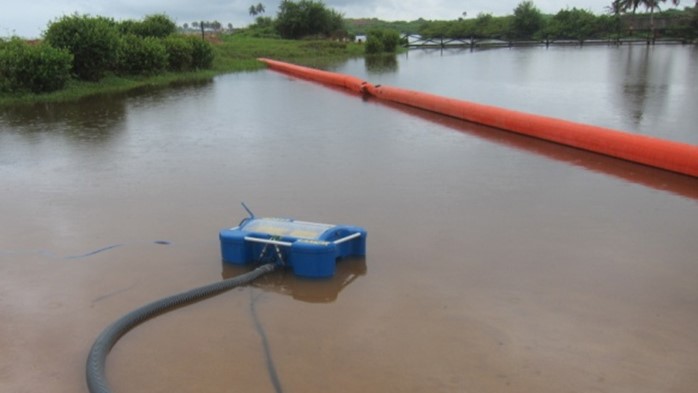 This image showcases a skimmer device actively deployed during Tullow Ghana Limited's oil spill response exercise, supported by OSRL. The skimmer is working alongside a bright orange containment boom, which is strategically placed to control the spread of oil in a shallow water environment. The exercise is part of a broader effort to enhance preparedness for oil spill incidents, ensuring rapid response capabilities.