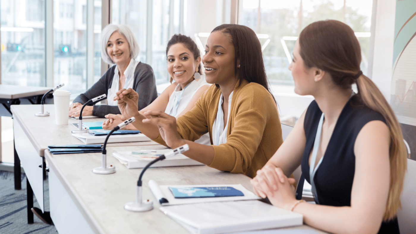 The image captures a professional setting where women leaders share insights and experiences in a panel discussion. It highlights the importance of representation, mentorship, and embracing femininity in leadership.