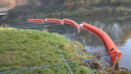 A containment boom deployed in an inland river to manage an oil spill. Proper boom placement is critical in slowing the spread of oil and allowing for efficient recovery operations.