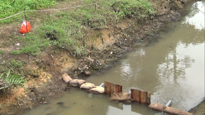 A controlled damming technique used to contain an oil spill in a small inland waterway. Sandbags and wooden barriers help slow oil movement, allowing for recovery and preventing further environmental damage.