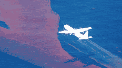 Aerial dispersant operations over the Montara spill site, showing a wide spread of oil sheen on the water surface.
