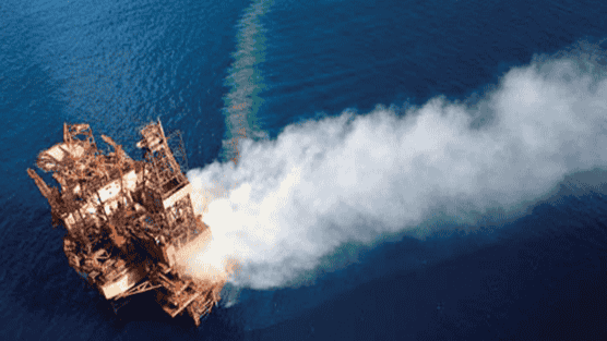 Aerial view of the Montara platform engulfed in smoke, with aircraft conducting dispersant application to mitigate the oil spill.