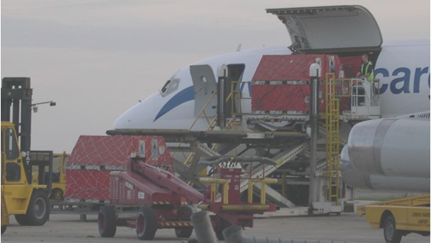  A cargo aircraft with its nose lifted, unloading red cargo containers using specialised lifting equipment, representing OSRL's role in logistics support during the MV Tasman Spirit response.