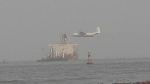 A Hercules aircraft flying low over the sea near a large vessel, deploying dispersant as part of oil spill response efforts during the MV Tasman Spirit incident.