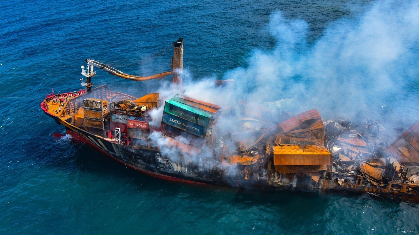 An aerial view of the X-Press Pearl ship after the fire, showing extensive damage and burnt cargo containers. The aftermath highlights the environmental impact of the incident, including the release of plastic pellets and hazardous substances into the ocean.