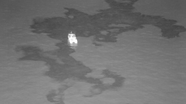 Infrared black-hot thermal image captured by UAV, highlighting oil spill extents around a response vessel during environmental monitoring.