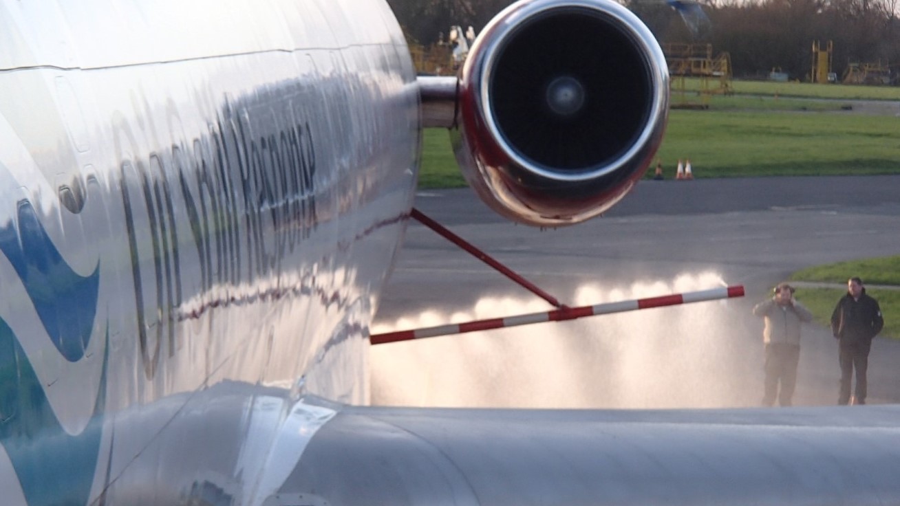 Rear view of the OSRL Boeing 727 during a ground dispersant spray demonstration. Visible dispersant mist and observer personnel reinforce operational realism.
