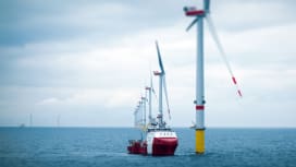  A large offshore wind farm with multiple turbines and a red support vessel navigating through the site.
