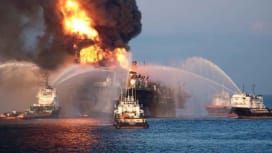 Multiple response vessels spraying water to suppress fires on a burning offshore rig.