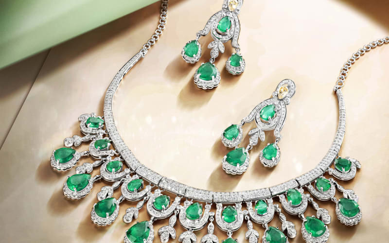 An emerald and diamond necklace with matching earrings laid on sage-green fabric.