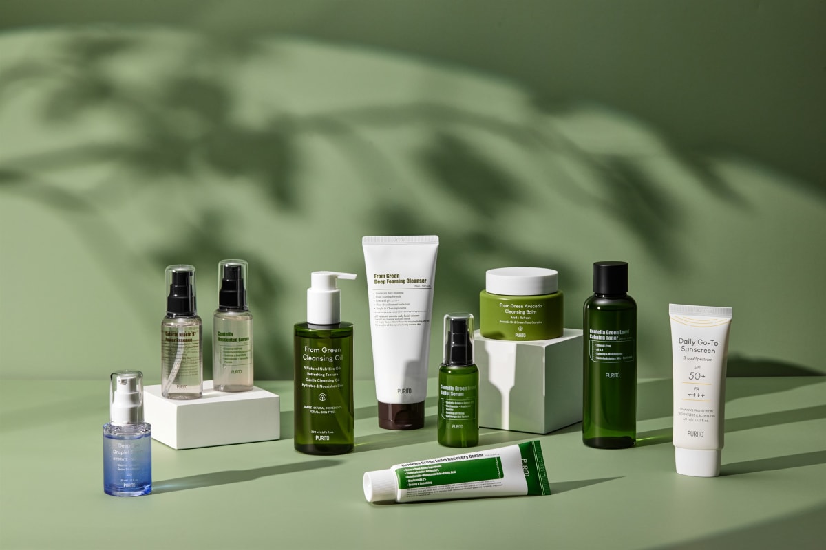 A ten-piece skincare line arranged on a green set under the shadow of a palm leaf.
