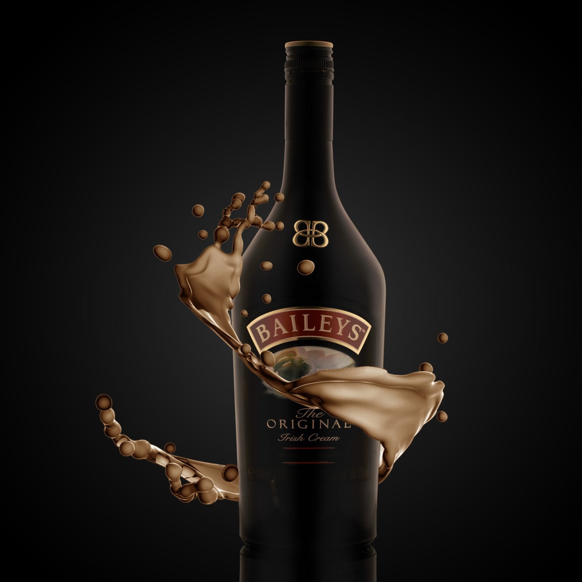 A dark drinks shot: a splash of cream liqueur frozen mid-air around a bottle.