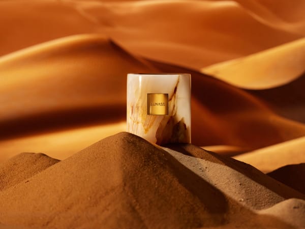 A marbled perfume bottle standing on a ridge of orange desert sand.