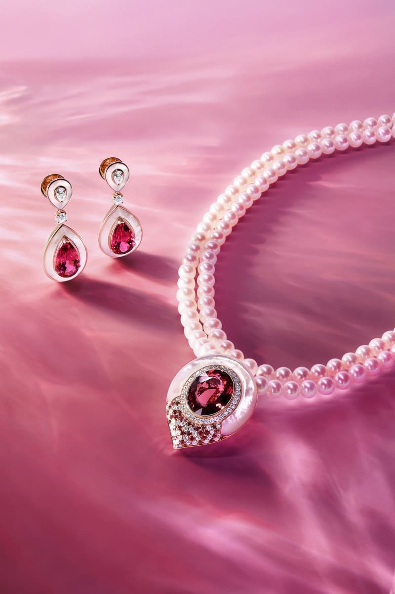 A pearl and ruby necklace laid across flowing pink fabric.