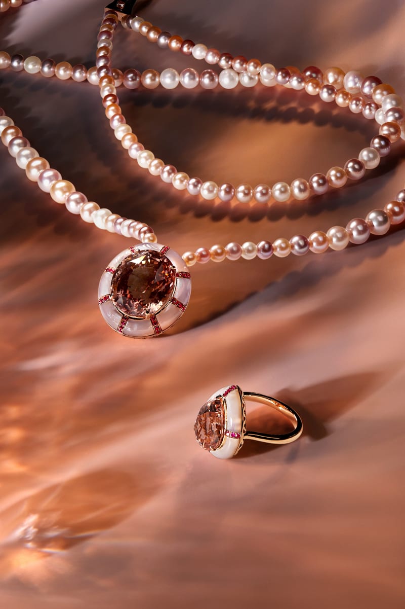 Earrings and pearls staged on a coloured surface.