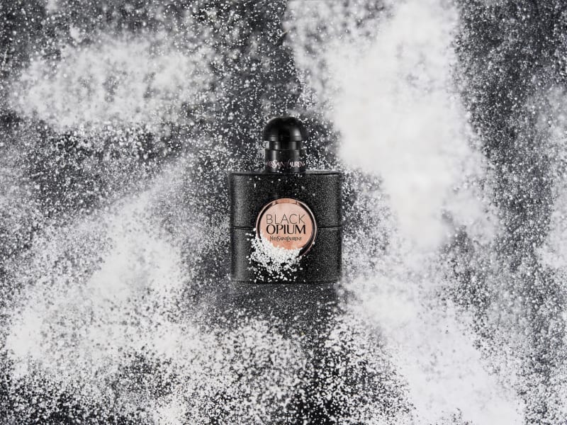 A dark perfume bottle at the centre of an explosion of white powder.