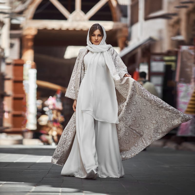 A model in a white embroidered abaya walking through a Dubai souk.