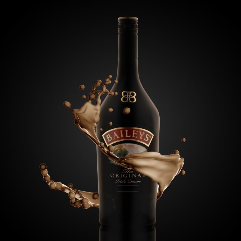 A splash of cream liqueur frozen mid-air around a dark bottle.