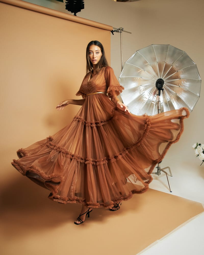 A model spinning in a tiered bronze tulle gown in the studio, a silver umbrella behind her.