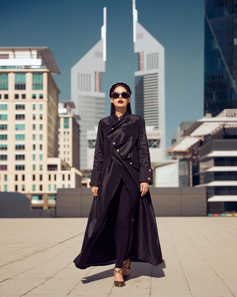 A model in a draped black coat and jewelled headband in front of the Emirates Towers.