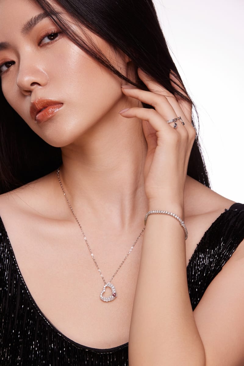 A delicate diamond pendant, tennis bracelet and ring worn against a light backdrop.