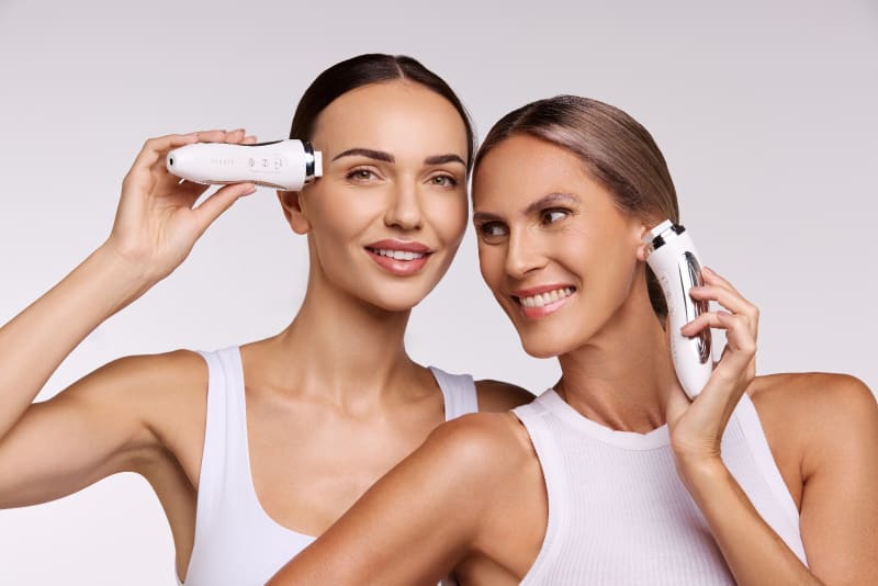 Two models holding beauty tech devices in a bright campaign frame.