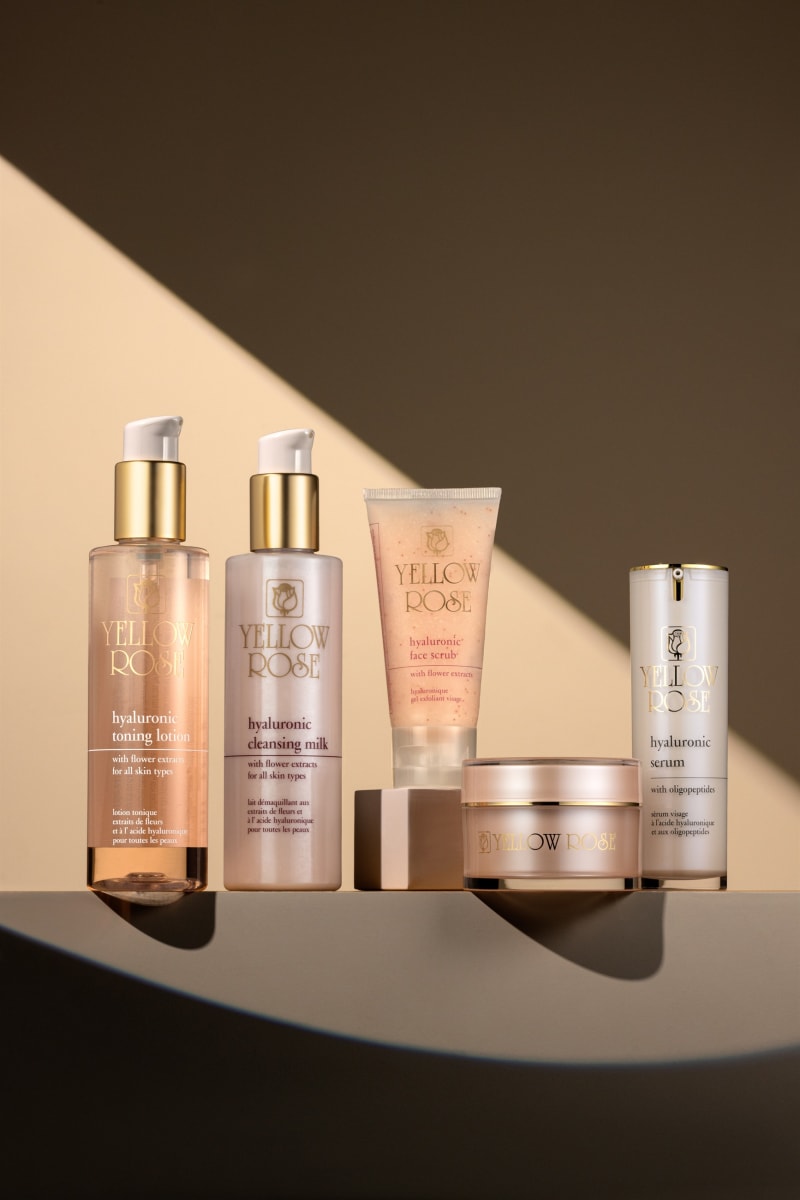 A five-piece skincare line lit by a hard diagonal of light on a curved beige set.