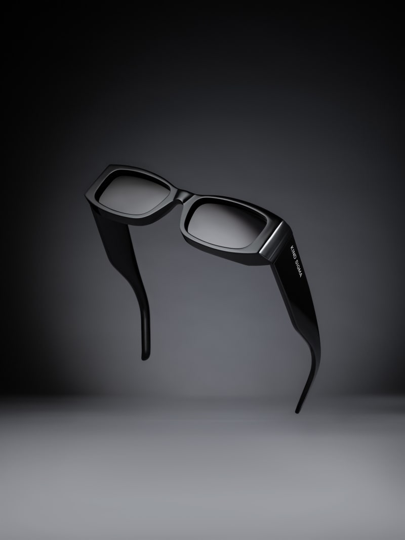 Black sunglasses suspended in mid-air above their own shadow on a graded dark backdrop.