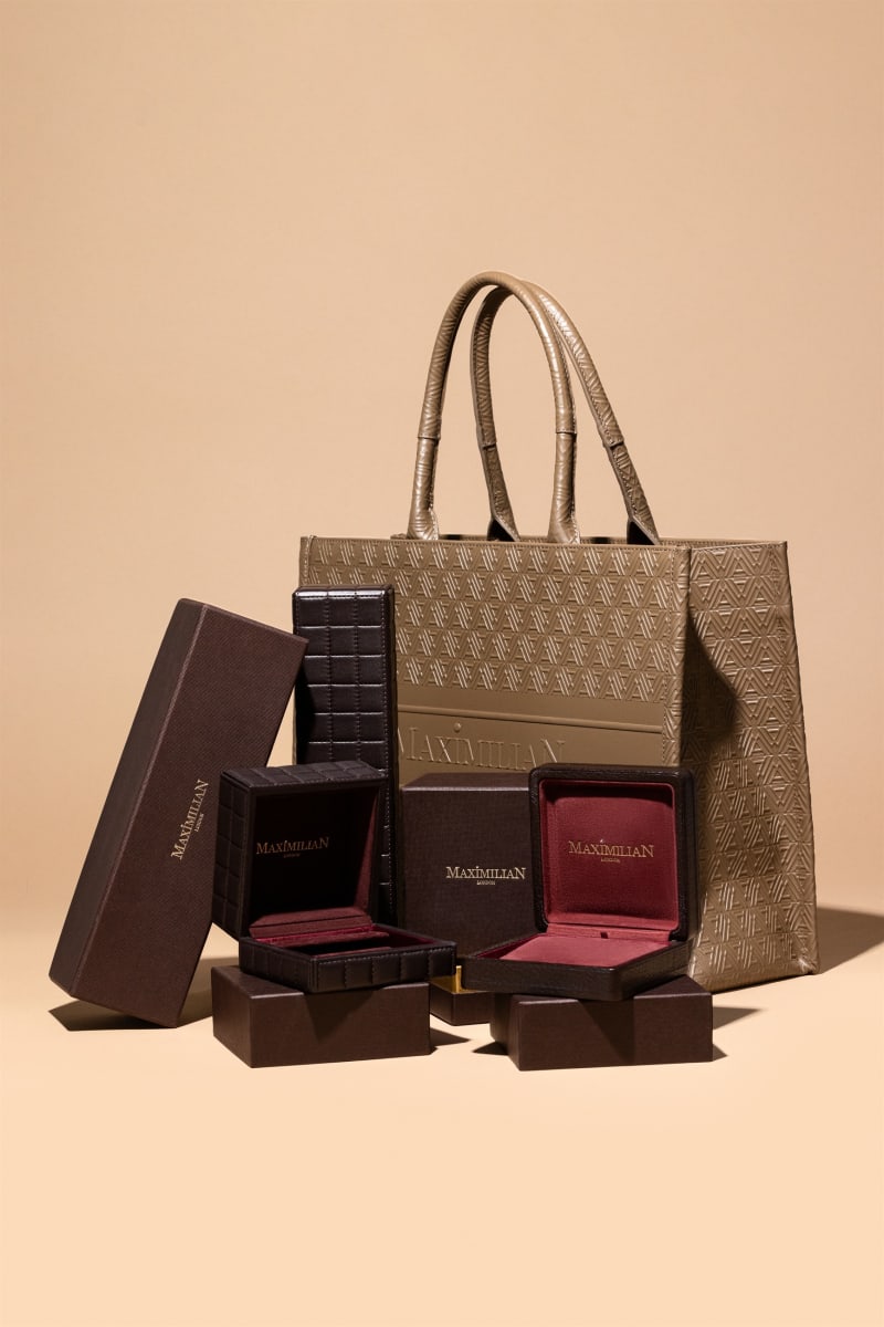 A brand's packaging family — boxes, jewellery cases and a monogram tote — arranged as one set on beige.
