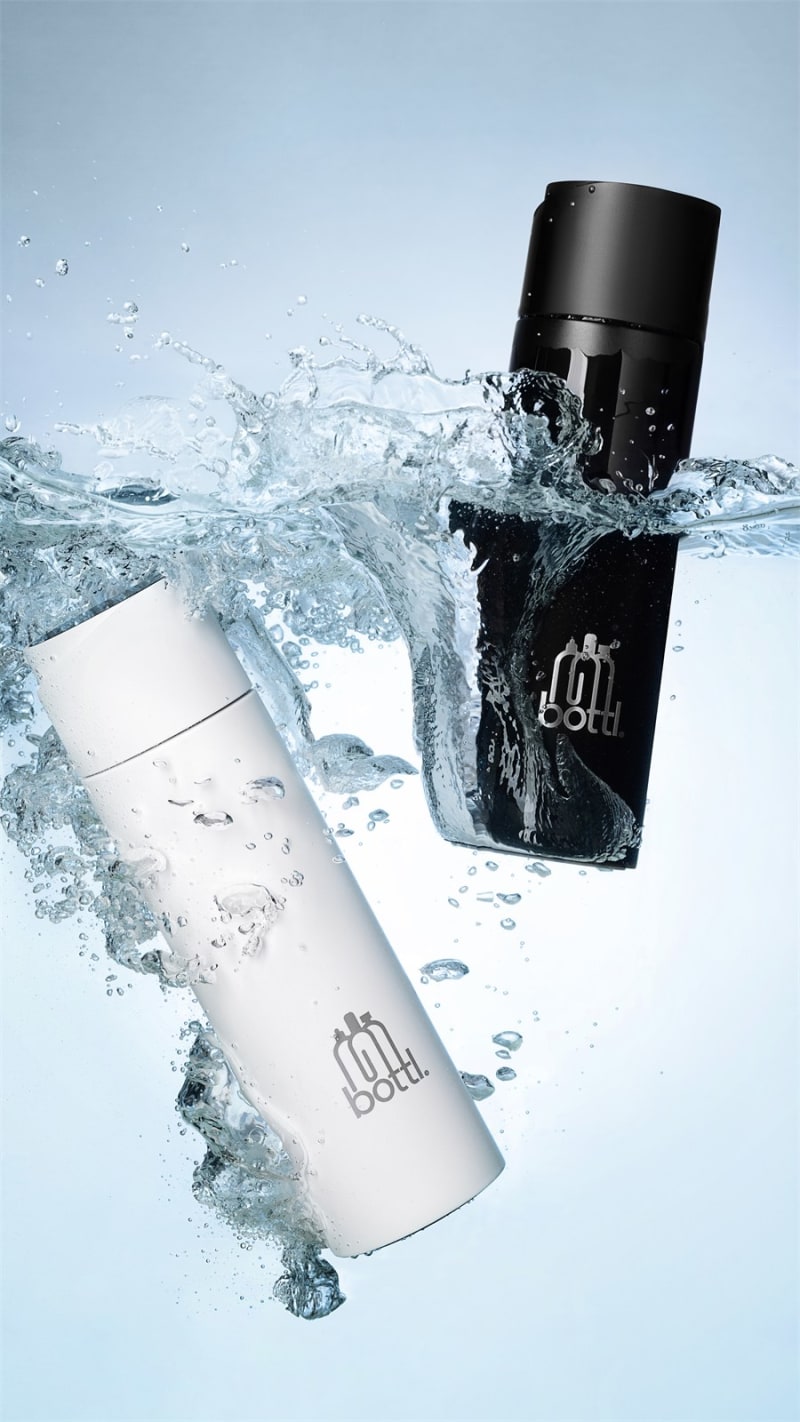 A black and a white insulated bottle suspended mid-splash underwater.
