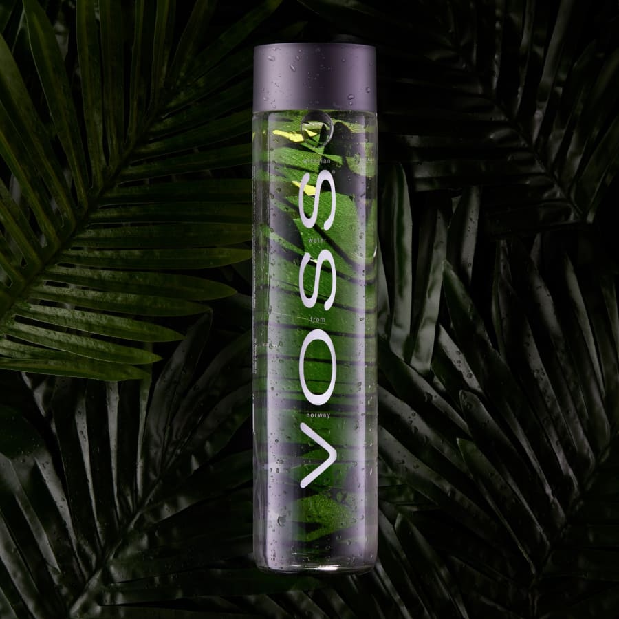 A water bottle laid over palm leaves with condensation droplets.
