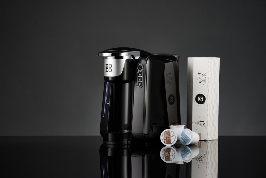 A coffee machine with capsules and packaging photographed on a dark set.