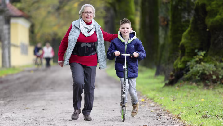 Christa mit Rückenorthese Dyneva spaziert mit ihrem Enkel durch einen Park.