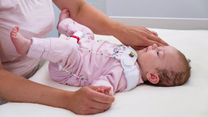 Tilda usa a órtese de flexão e abdução de quadril de Tubingen enquanto está deitada na mesa de troca de fraldas.